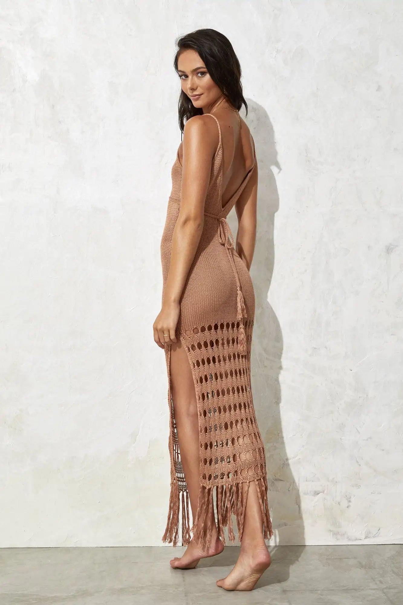 Woman wearing a beige fringe cover up dress against a white wall