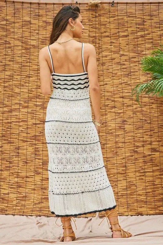 Woman wearing a black and white patterned vacation beach dress against a woven wall.