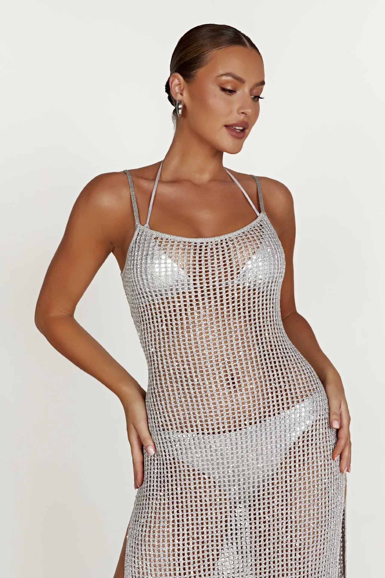 Woman wearing a silver cover up high slit dress against a white background