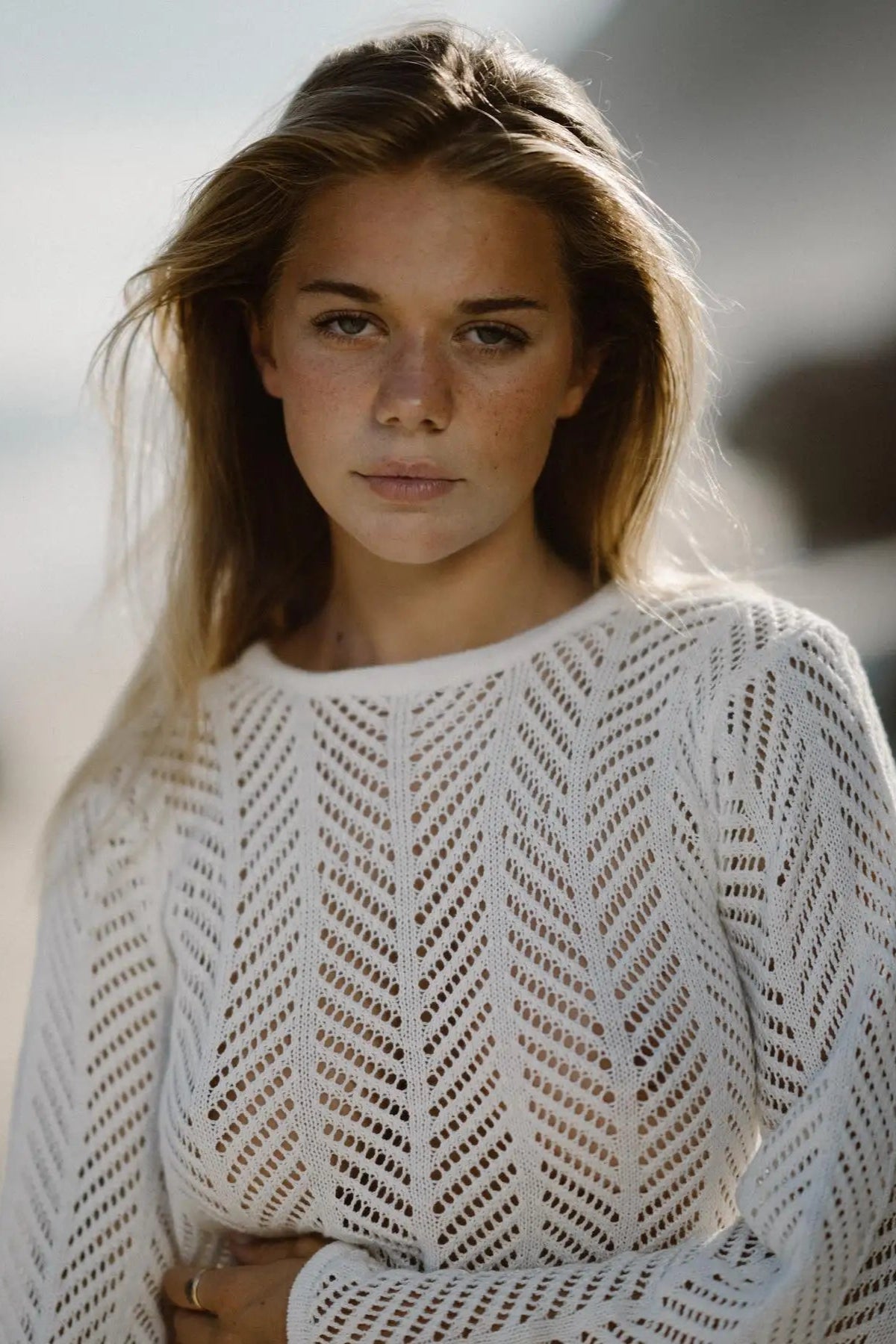 Woman wearing a white knit cover up on a blurred natural background