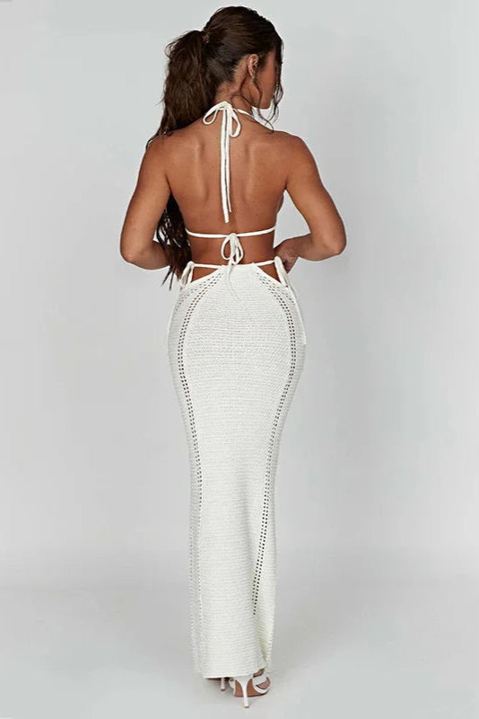 Woman wearing a white open-back bikini top and cover up skirt on a plain background