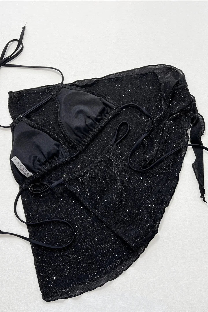 A black strappy bikini top and matching bottoms set and cover up sarong with a textured, glittery fabric