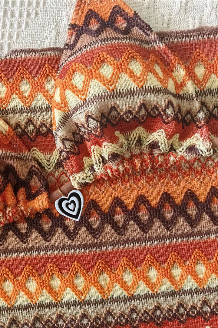 A close-up of a knit fabric with a geometric Fair Isle pattern in orange, brown, beige, and cream, featuring a small white heart-shaped graphic overlay.