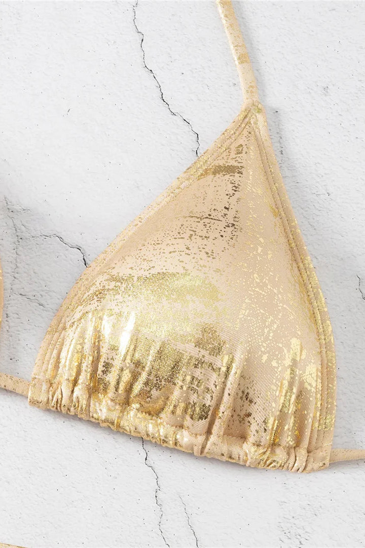 A close-up of a metallic gold triangle bikini top with a fringed underband