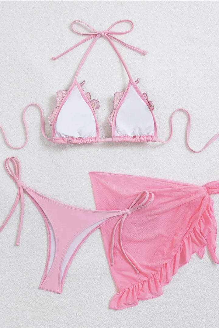 A pink padded two-piece bikini set with a matching pink swim sarong. The bikini top has white triangle cups while the matching bikini bottom is thong-style with pink ruffle trim.