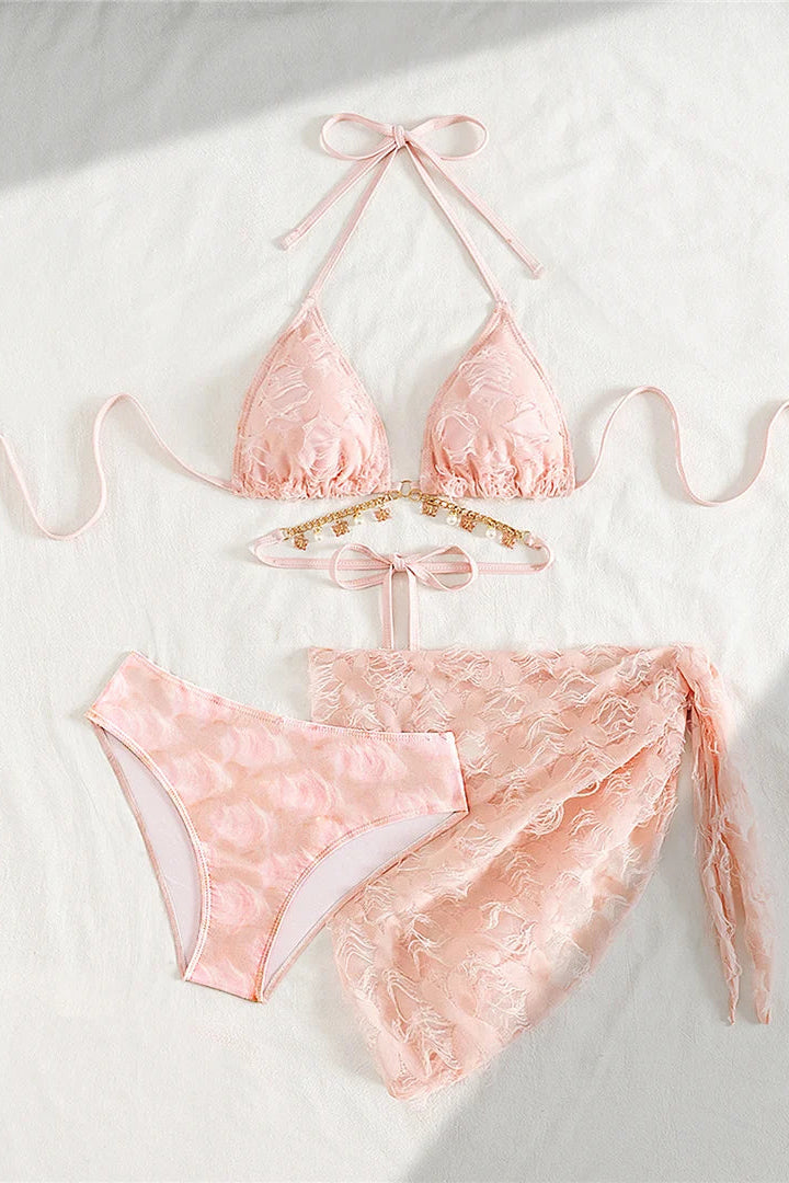 A three-piece light pink swimwear set includes a triangle bikini top with long ties, matching bikini bottoms, and a sheer lace wrap sarong tied at the waist.