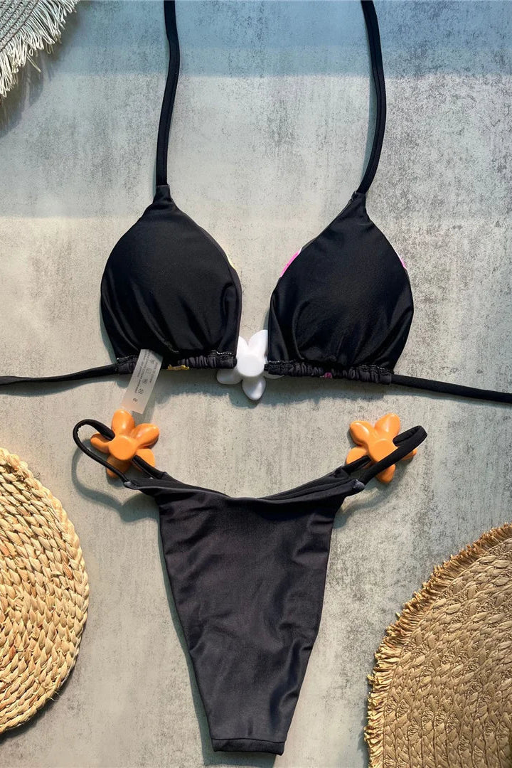 A two-piece bikini set featuring a bandeau-style triangle top with thin straps and a matching low-rise thong bottom with orange flower-shaped accents on the side straps.