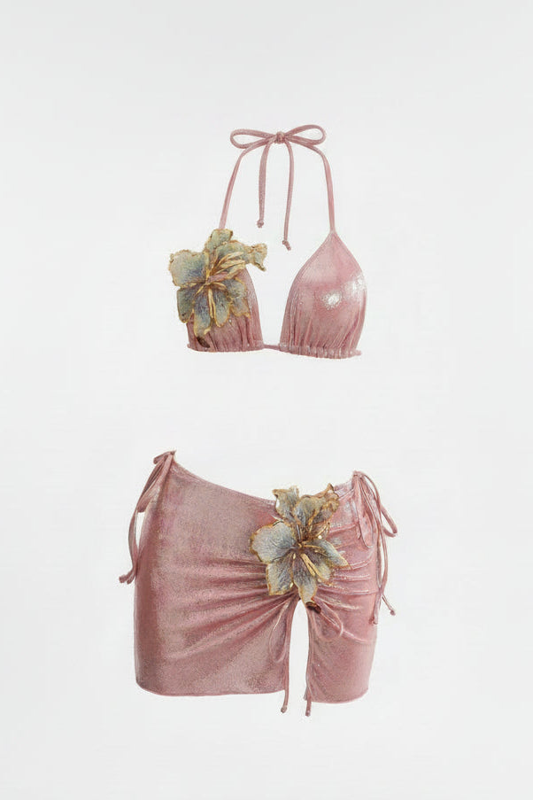 A two-piece bikini set in a dusty rose pink fabric, featuring a halter top with floral applique and matching ruched side-tie bottoms with a large flower detail
