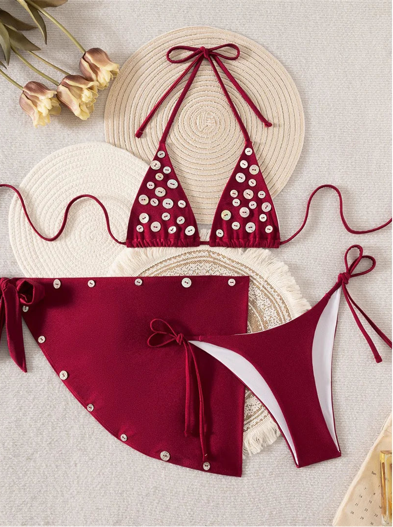 A two-piece bikini set in deep burgundy red, decorated with white and silver buttons. The set includes a halter triangle top and matching tie-side bottoms and mini sarong