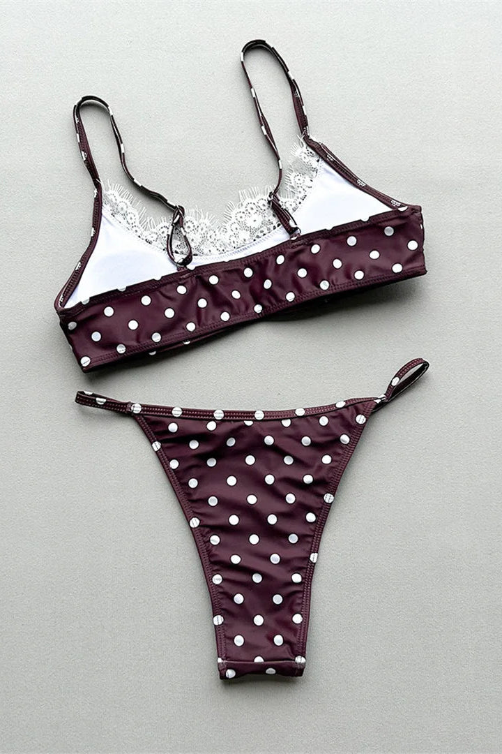 A two-piece bikini set laid flat on a light gray background. The bikini top is burgundy with white polka dots and a white lace underband, while the matching bikini bottom is solid burgundy with white polka dots.