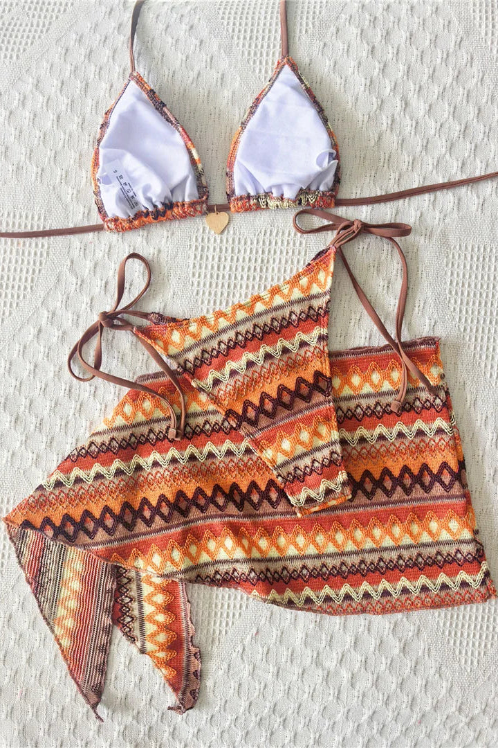 A two-piece bikini set with a matching patterned sarong, The bikini top has light lavender-purple triangles with orange and brown patterned edges and thin brown ties.