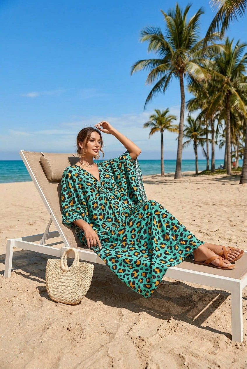 A woman on a beach wearing a flowing caftan-style dress with a turquoise, black, and orange leopard print