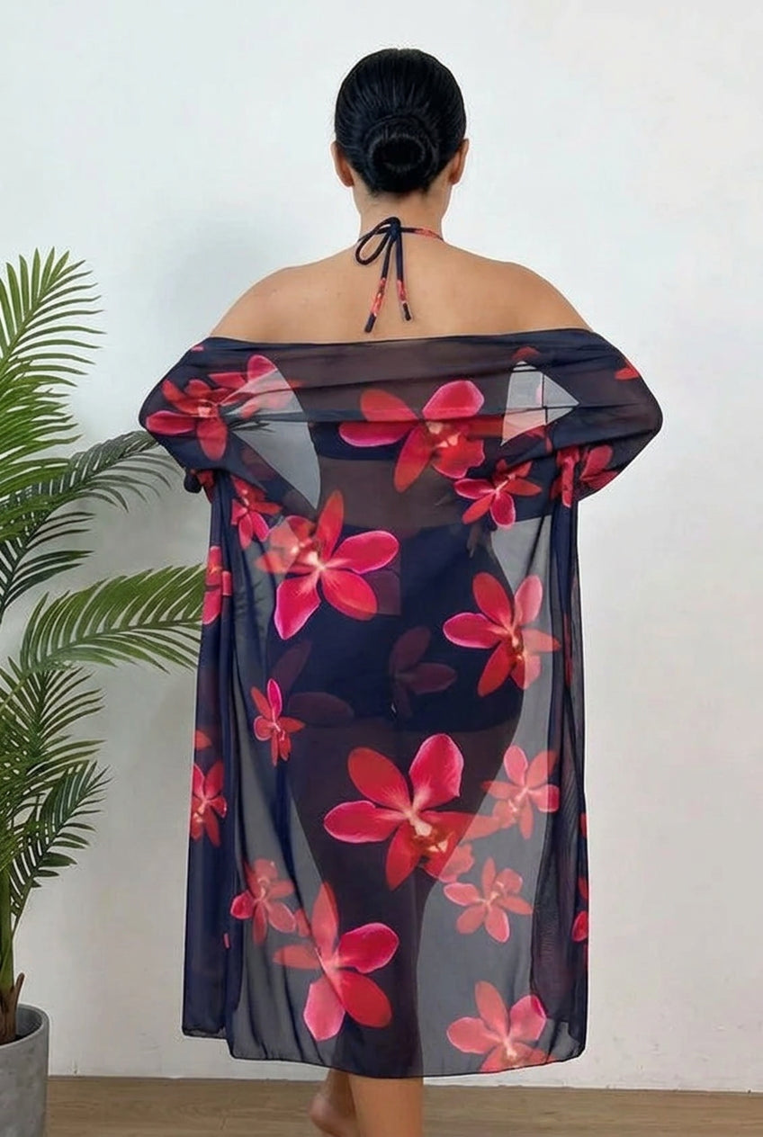 A woman viewed from behind wearing a sheer off-the-shoulder cover-up and bikini set with a vibrant pink and red floral print on a dark navy background