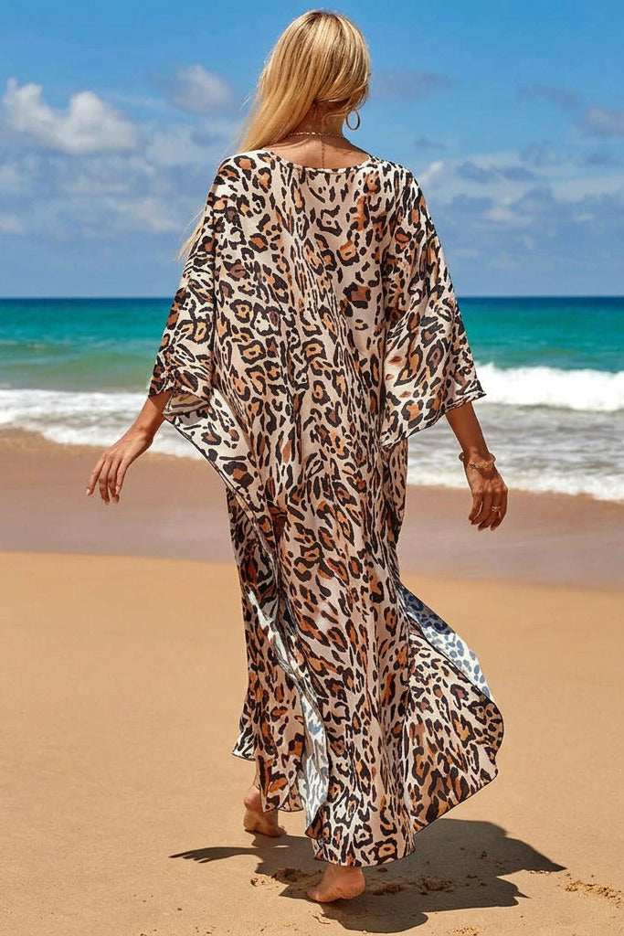 A woman walking on a sandy beach away from the camera, wearing a flowing leopard-print kaftan dress with wide three-quarter sleeves. 