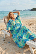 A woman wearing a flowing V-neck beach cover-up dress with a blue and green tie-dye pattern