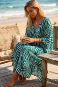A woman wearing a flowing maxi cover-up dress with a green and white zebra-like abstract pattern