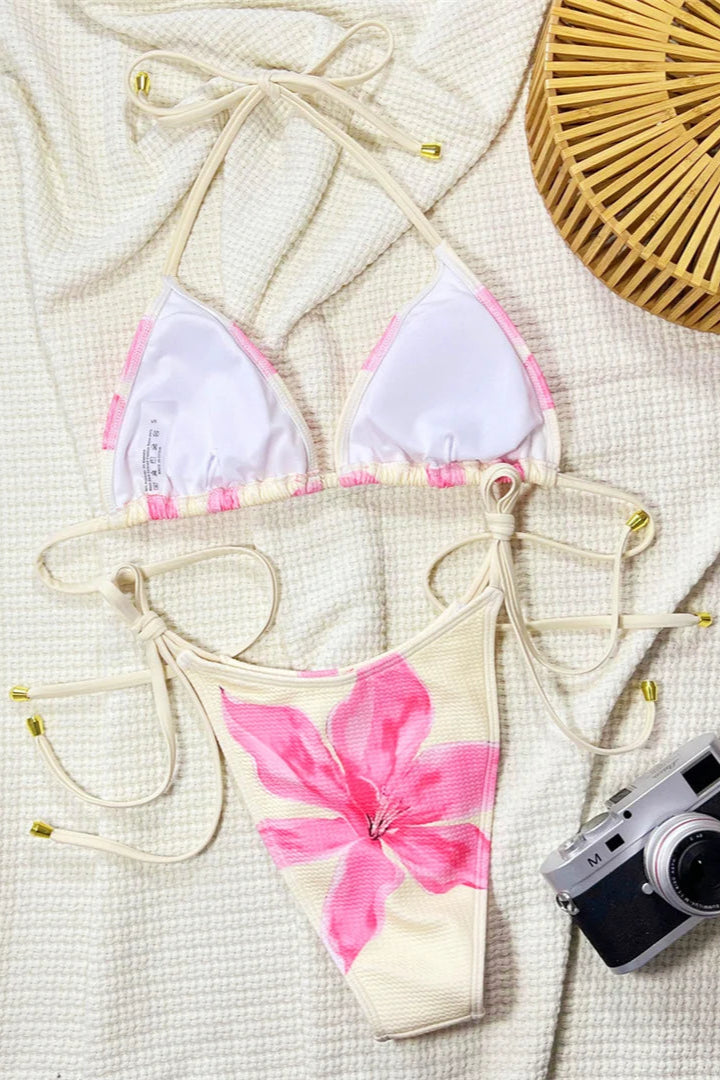 Bikini set with pink floral design on a textured surface with a camera and basket.