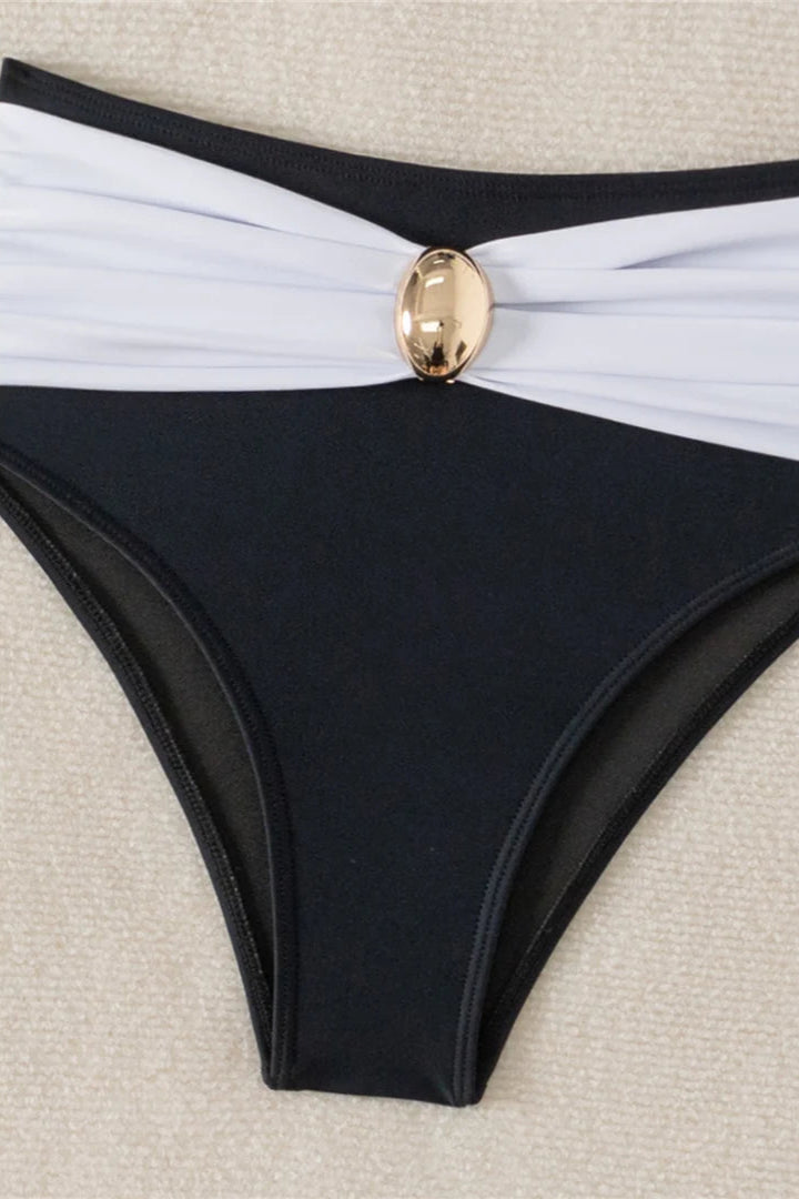Black bikini bottom with white waistband and gold button on a beige background