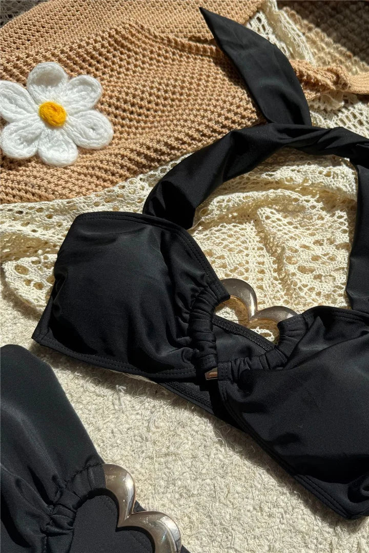 Black bikini set on a textured surface with a straw bag and flower decoration.