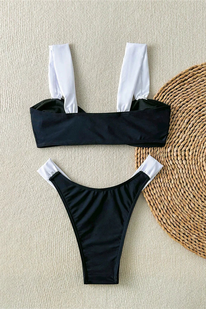 Black bikini set with white trim on a textured beige surface