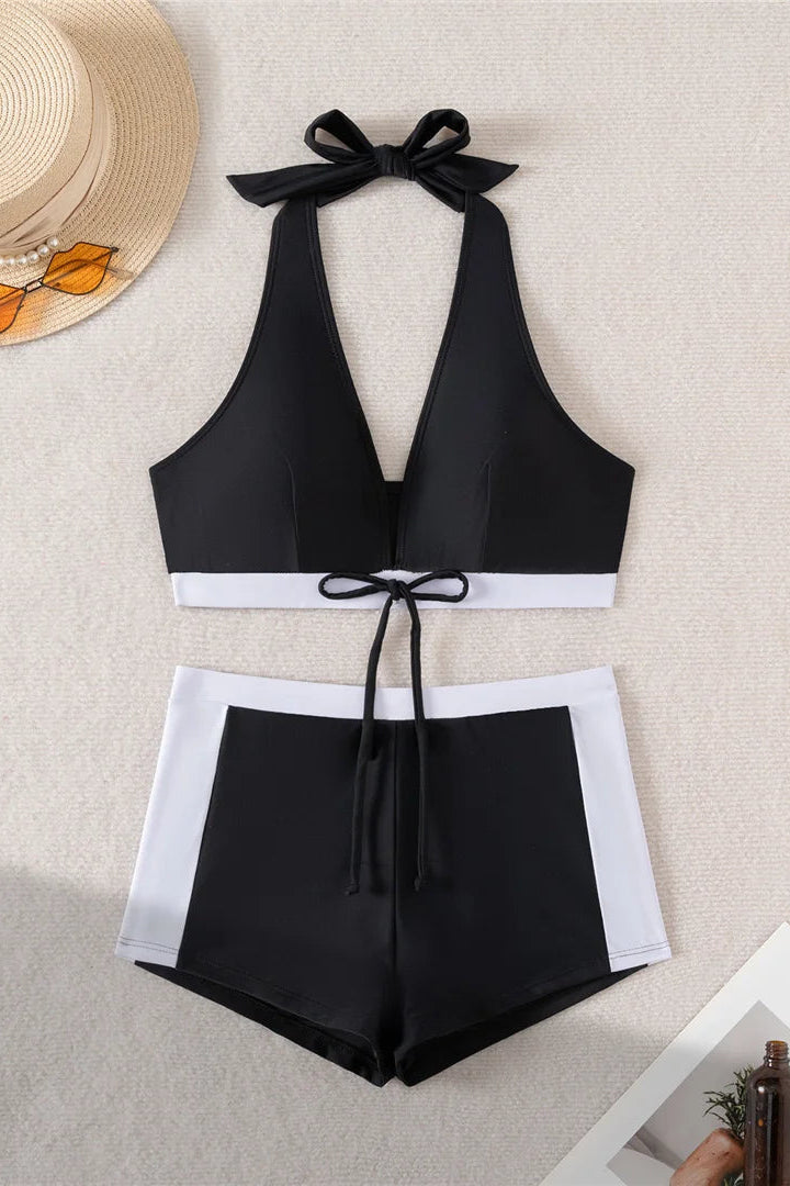Black bikini set with white trim on a textured surface with a hat and bottle in the background.