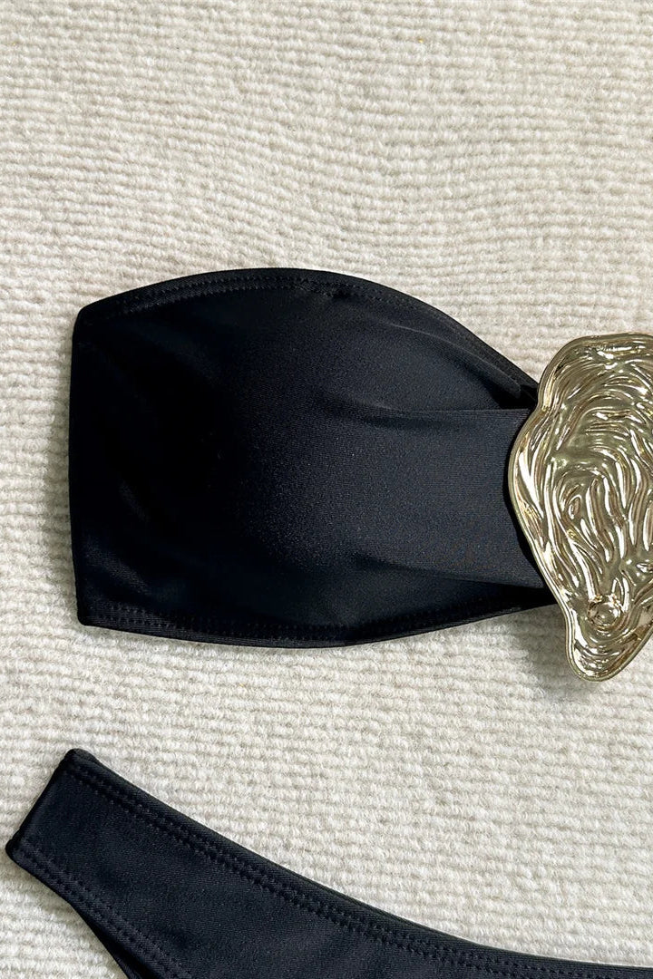 Black strapless bikini top with a decorative silver buckle on a textured beige surface