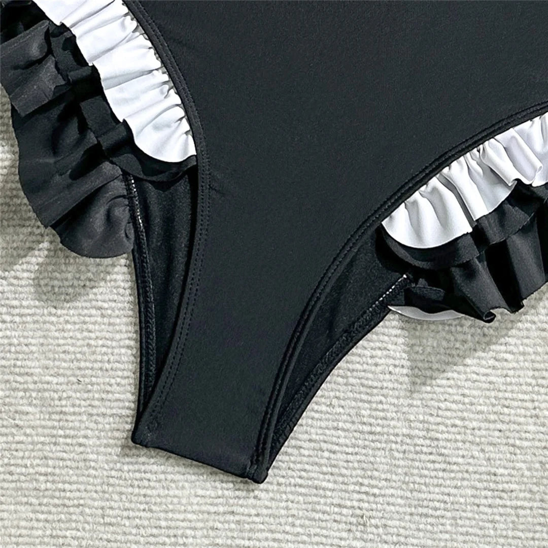 Black swimsuit with ruffled details on a textured surface