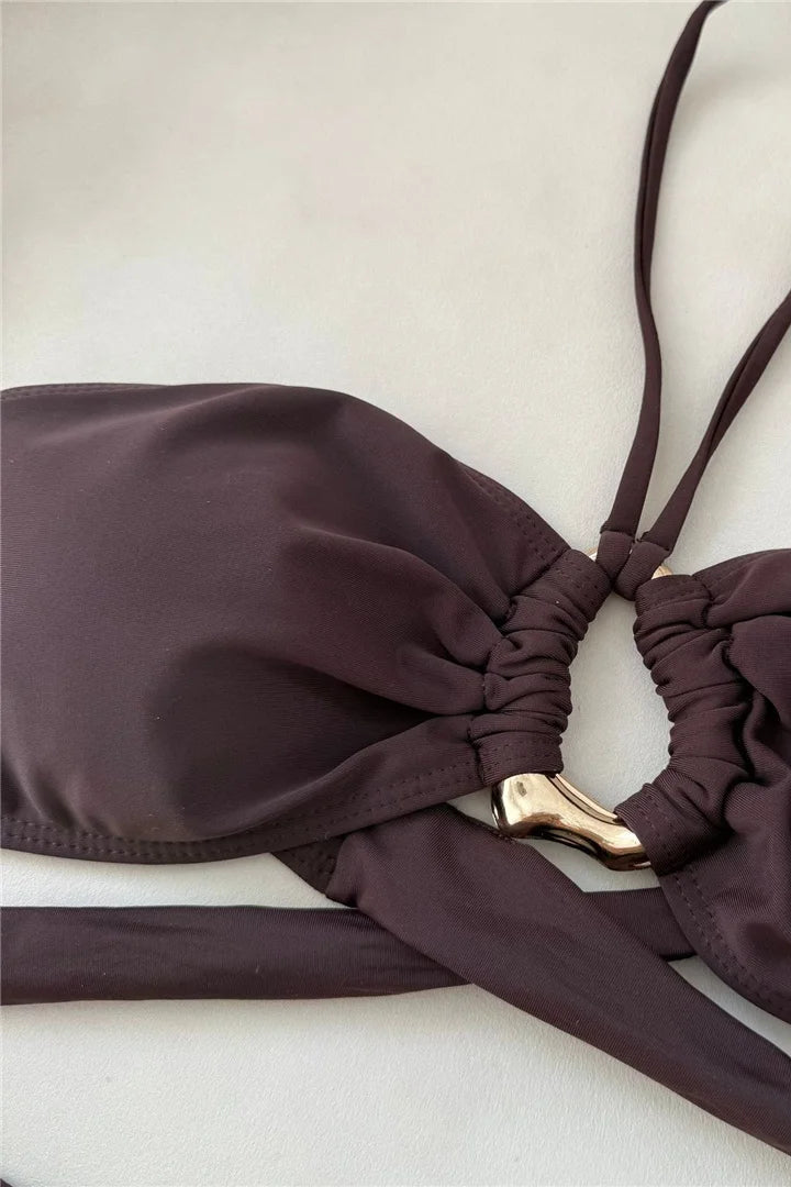 Brown bikini top with a gold clasp on a light background