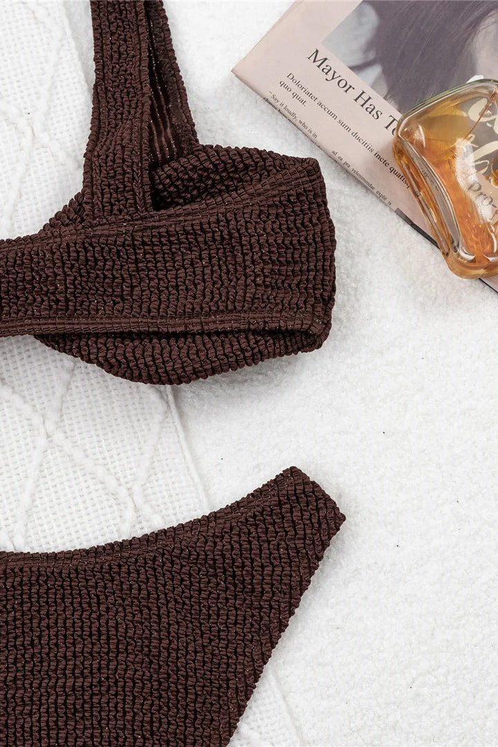 Brown crochet bikini set on a white surface with a magazine and glass.