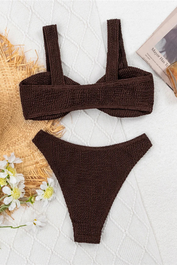 Brown knitted bikini set on a textured white surface with flowers and a book.