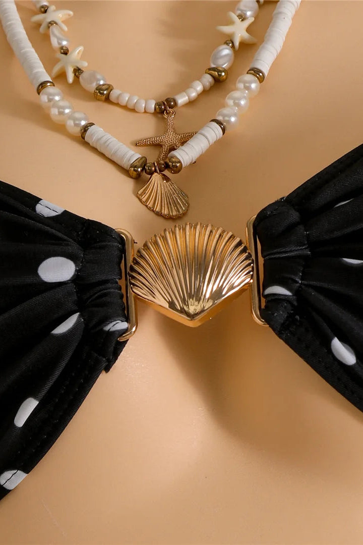 Close-up of a bikini top with black fabric panels featuring white polka dots, a metallic gold shell-shaped center clasp.