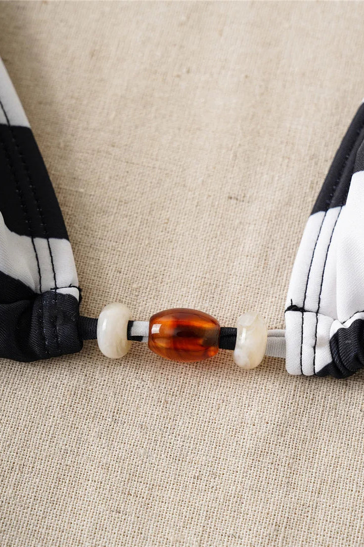 Close-up of a black and white striped bikini with a brown cylindrical object on a beige fabric background