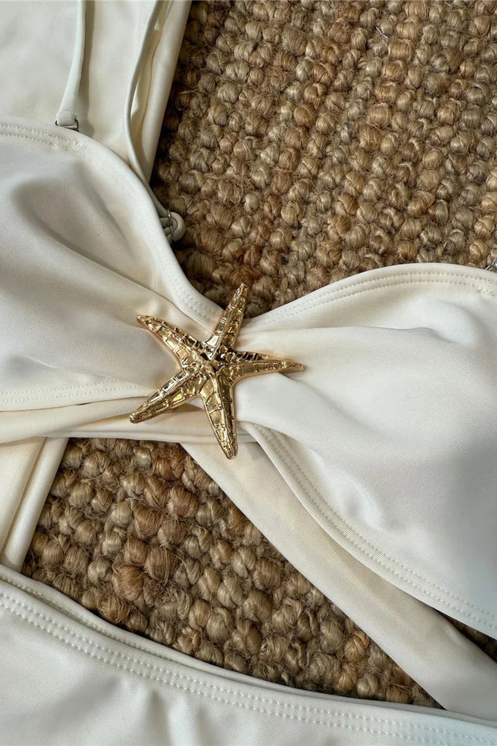 Close-up of a white garment with a gold starfish accessory on a textured brown surface