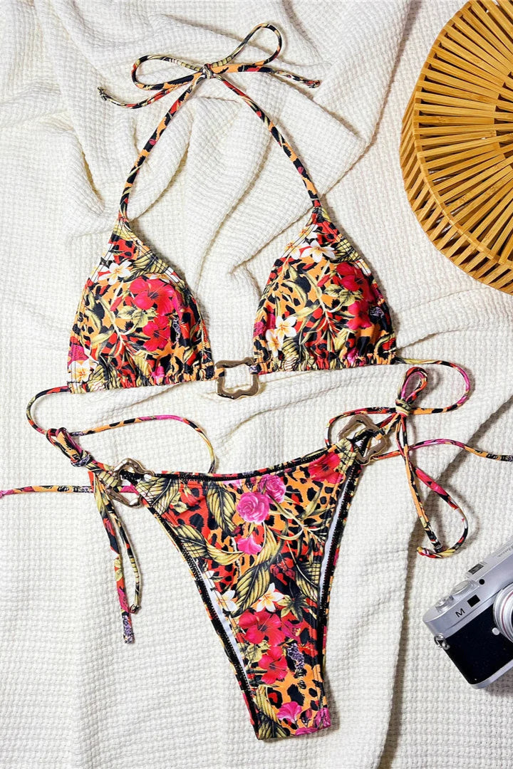 Colorful floral bikini set on a textured surface with a camera and fan in the background.