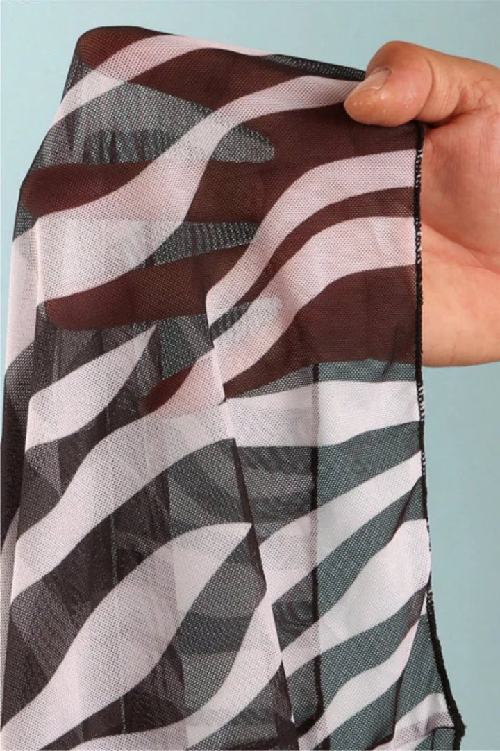 Hand holding a zebra striped fabric with brown, white, and gray pattern against a light blue background