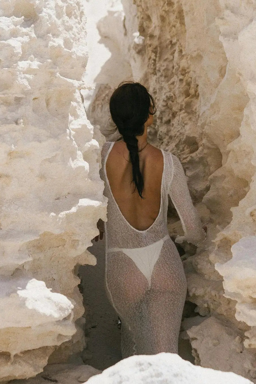 Person in a white swimsuit cover up standing against a textured white wall