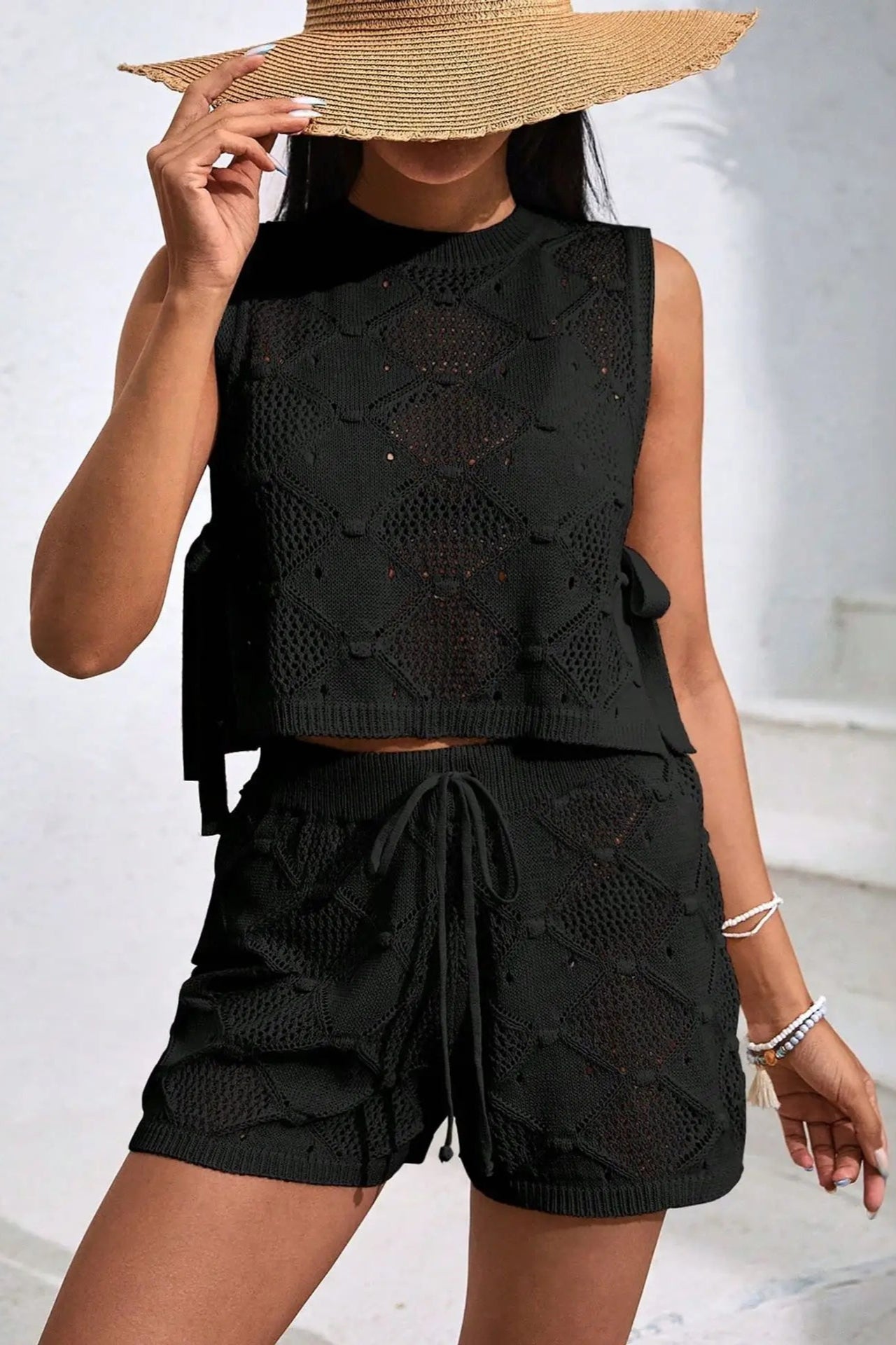 Person wearing a black sleeveless top and shorts cover up set with a straw hat.