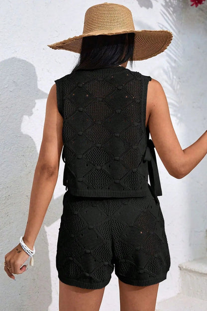 Person wearing a black sleeveless top and shorts with a straw hat, standing against a white wall.