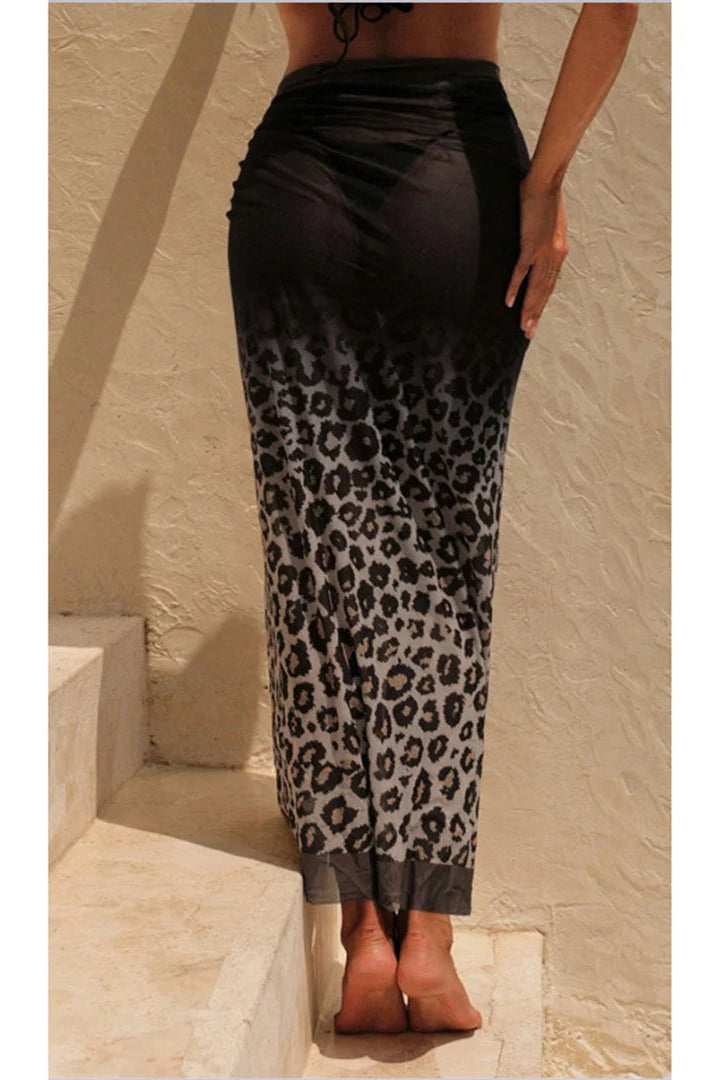 Person wearing a black top and leopard print pants against a beige wall.