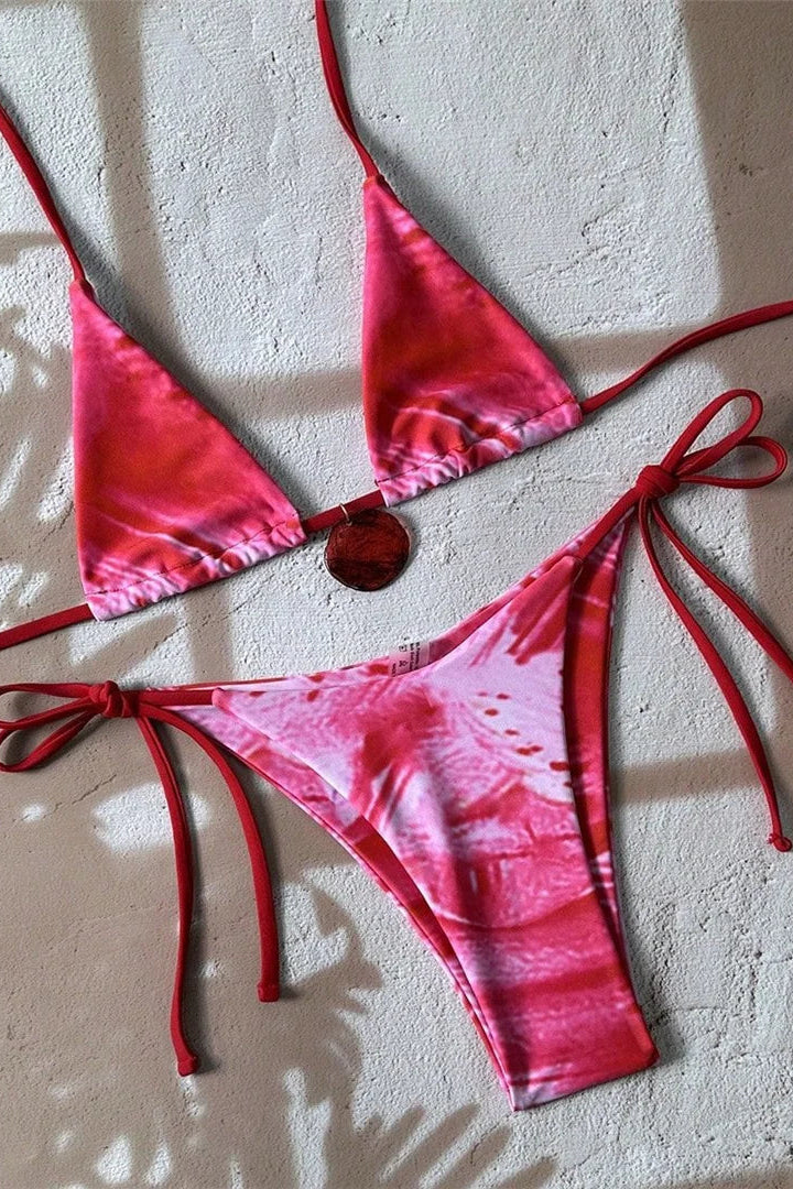 Pink tie-dye bikini set with red straps on a textured beige surface