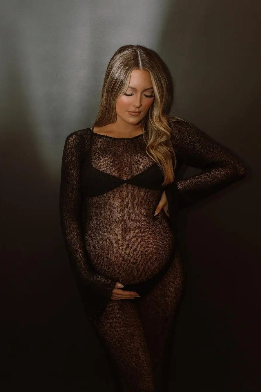 Pregnant woman wearing a sheer black cover up against a dark background