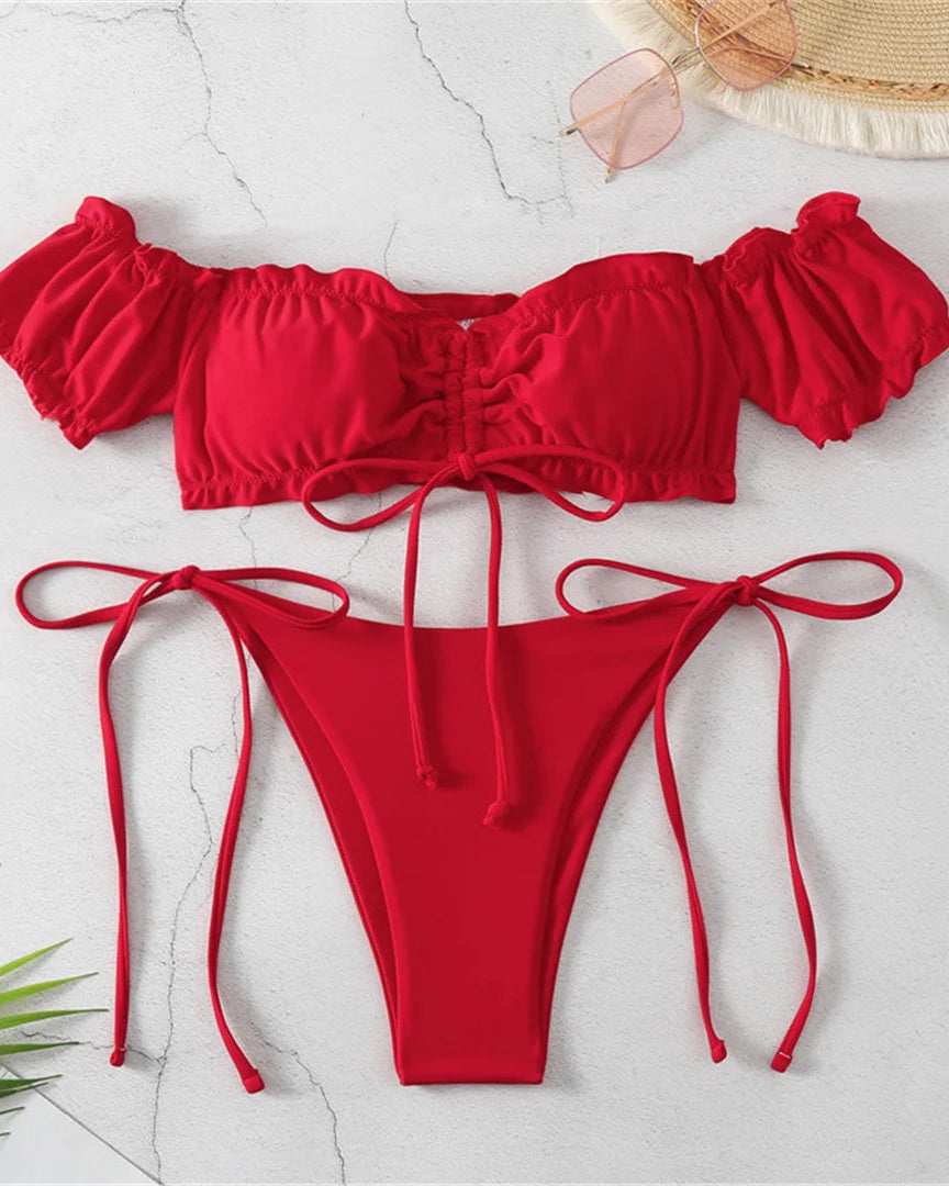 Red off shoulder bikini set on a light gray surface with a straw hat and sunglasses.