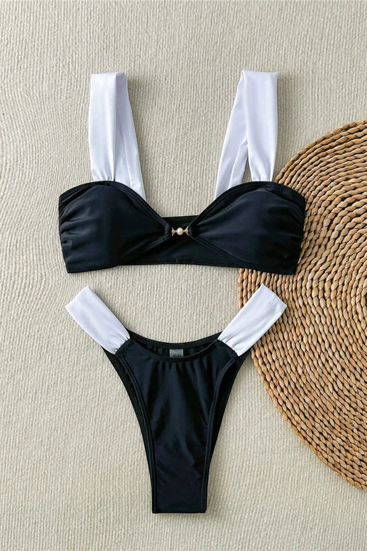 Black bikini set with white straps on a textured beige surface with a woven mat.