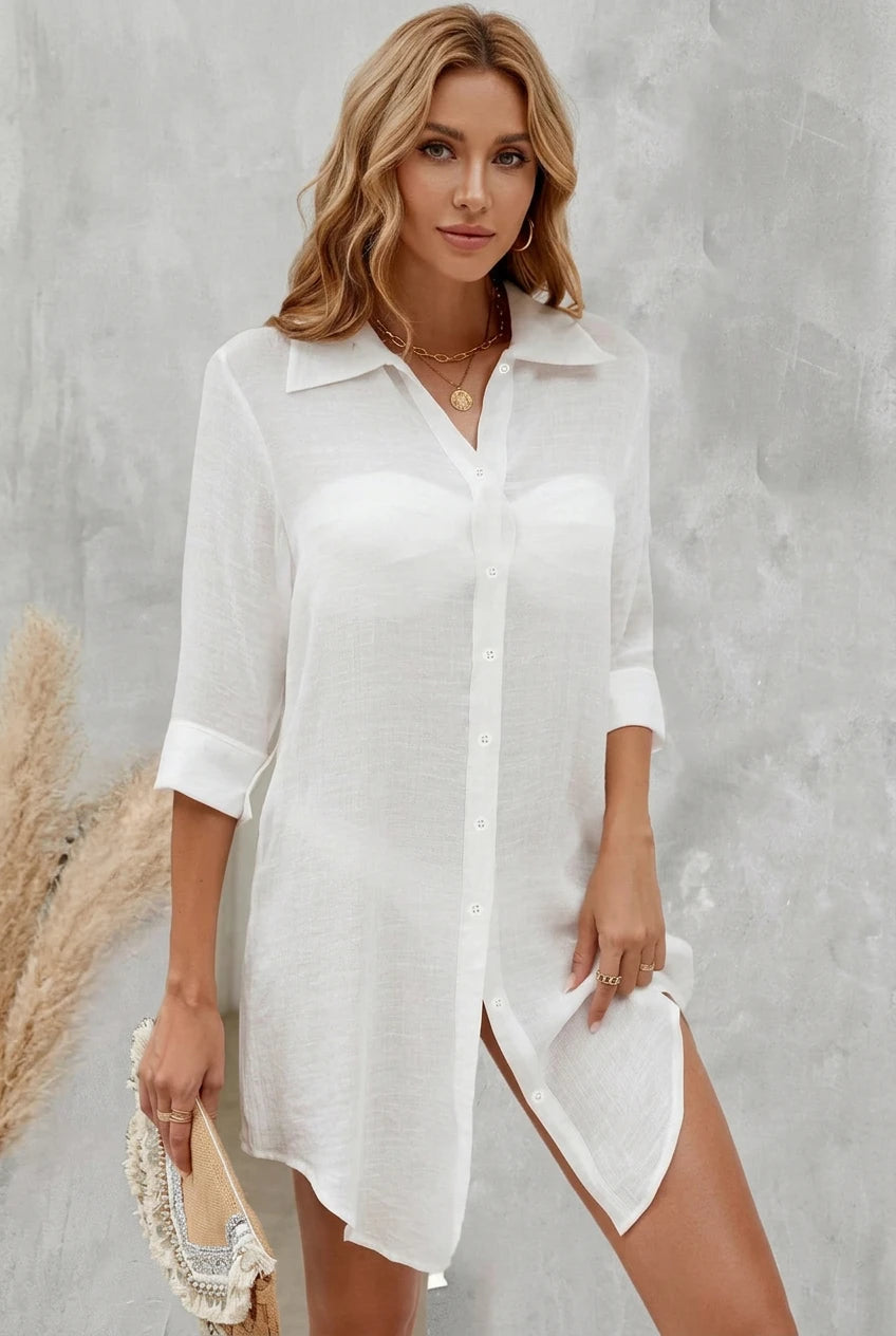 A woman wearing a white long-sleeve button-up shirt dress with a high-low hem and side slit.