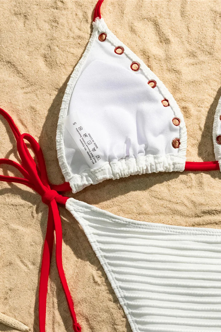 White bikini top with red straps on a sandy background