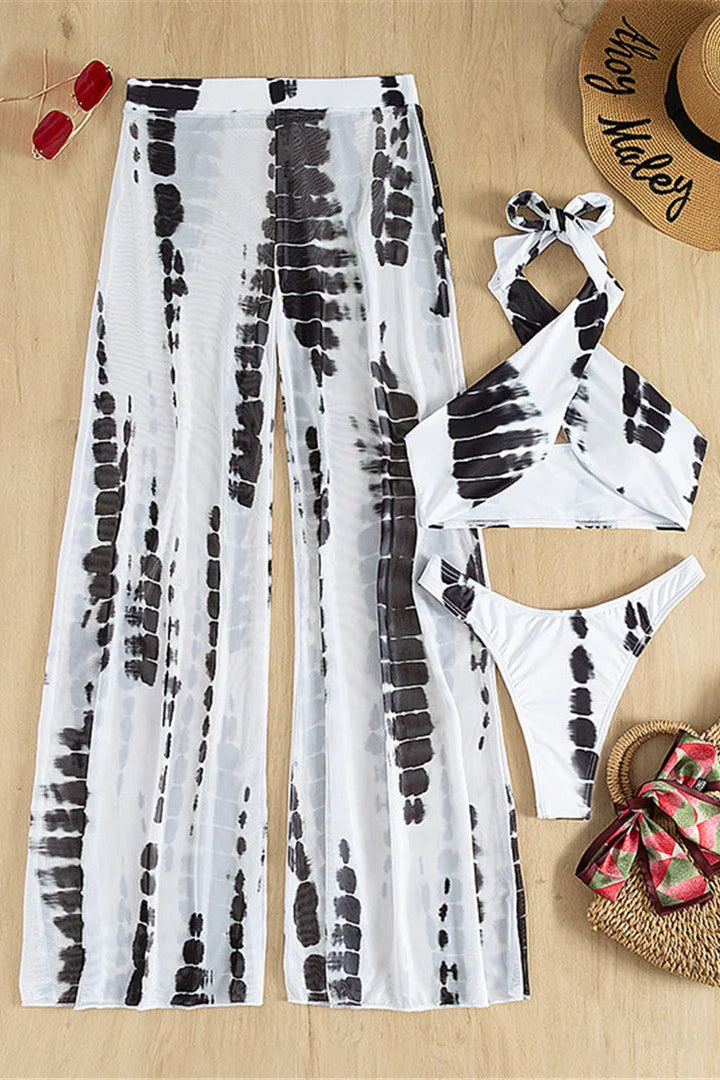 Tie-dye cover up pants and bikini set with straw bag and hat on a wooden surface