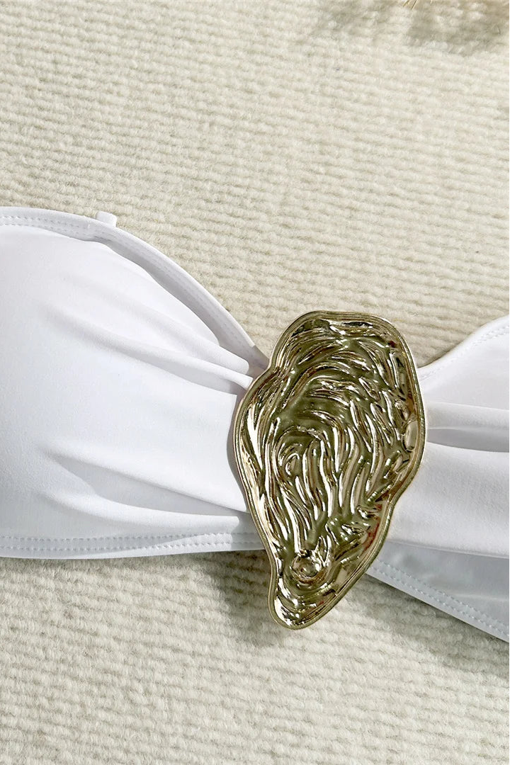 White bandeau top with a gold shell-like brooch on a textured beige surface