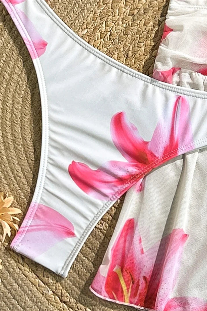 White bikini bottom with pink floral design on a woven surface with flowers.