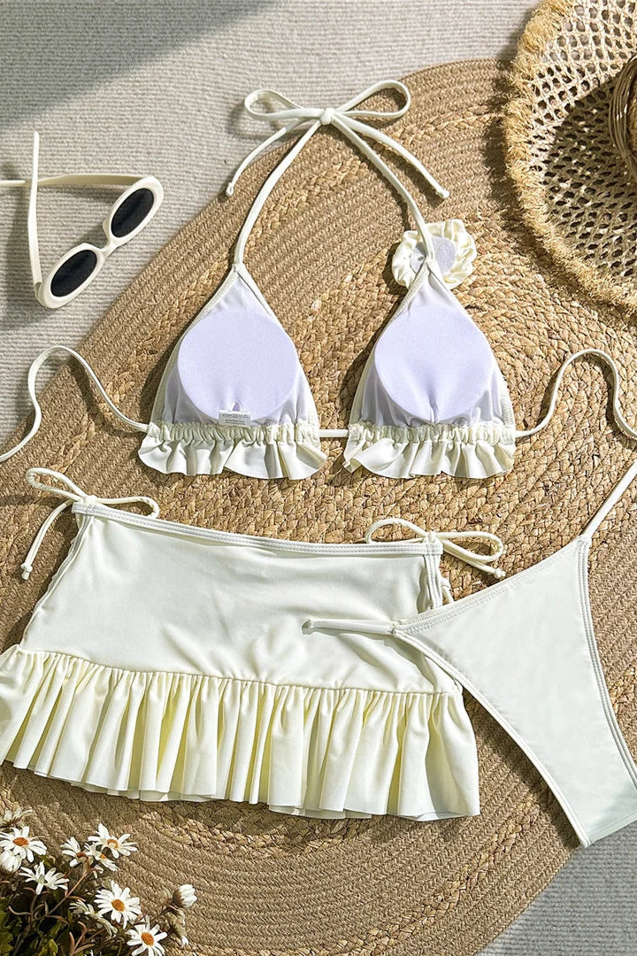 White bikini set with ruffled details on a woven mat with a straw hat and sunglasses.