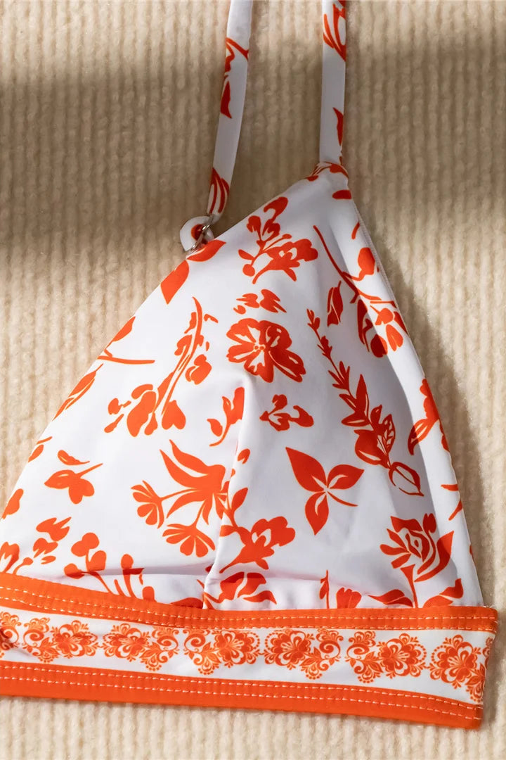 White bikini top with orange floral pattern on a beige textured background